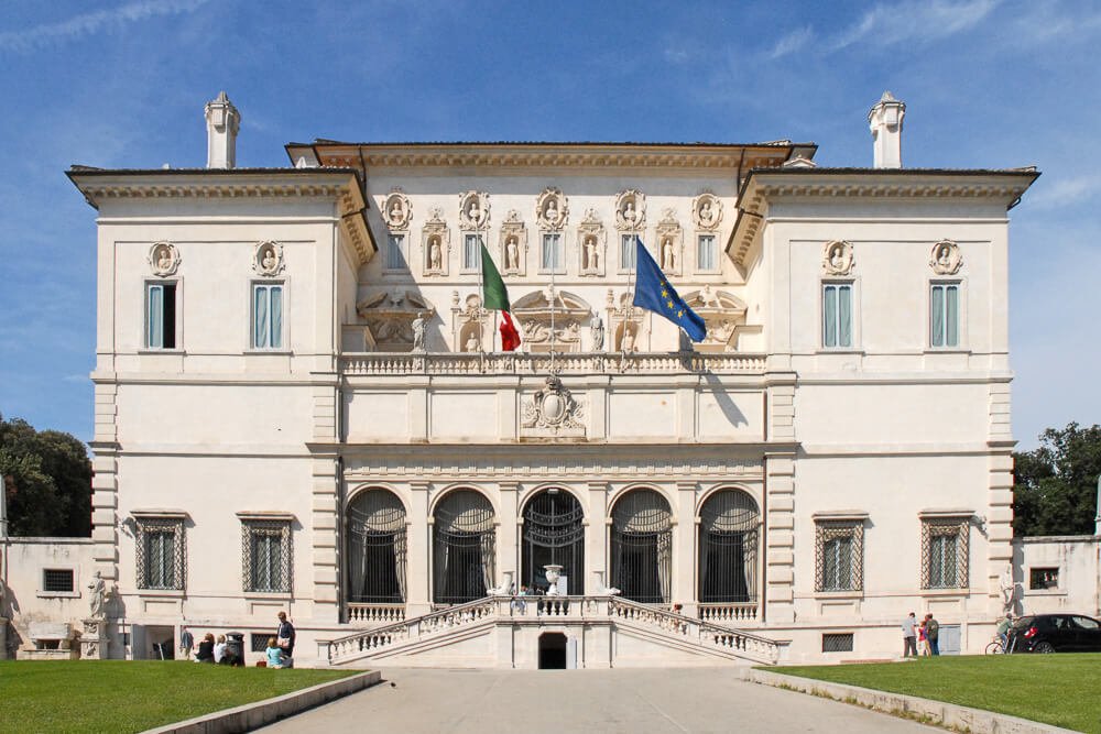 Galeria Borghese com gramados nas laterais e bandeiras hasteadas na fachada do edifício da galeria.