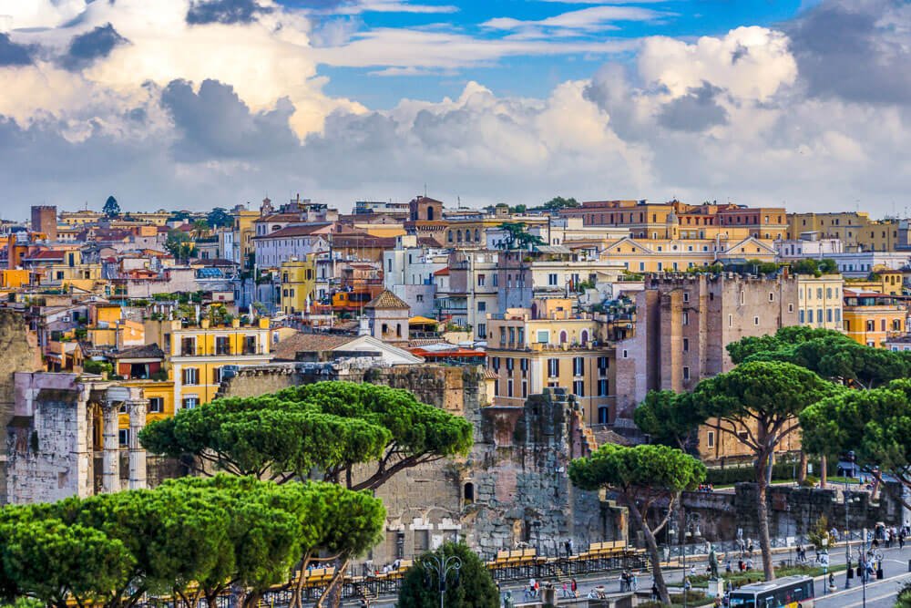 Vista superior para a cidade de Roma com prédios coloridos, árvores e algumas ruínas históricas.