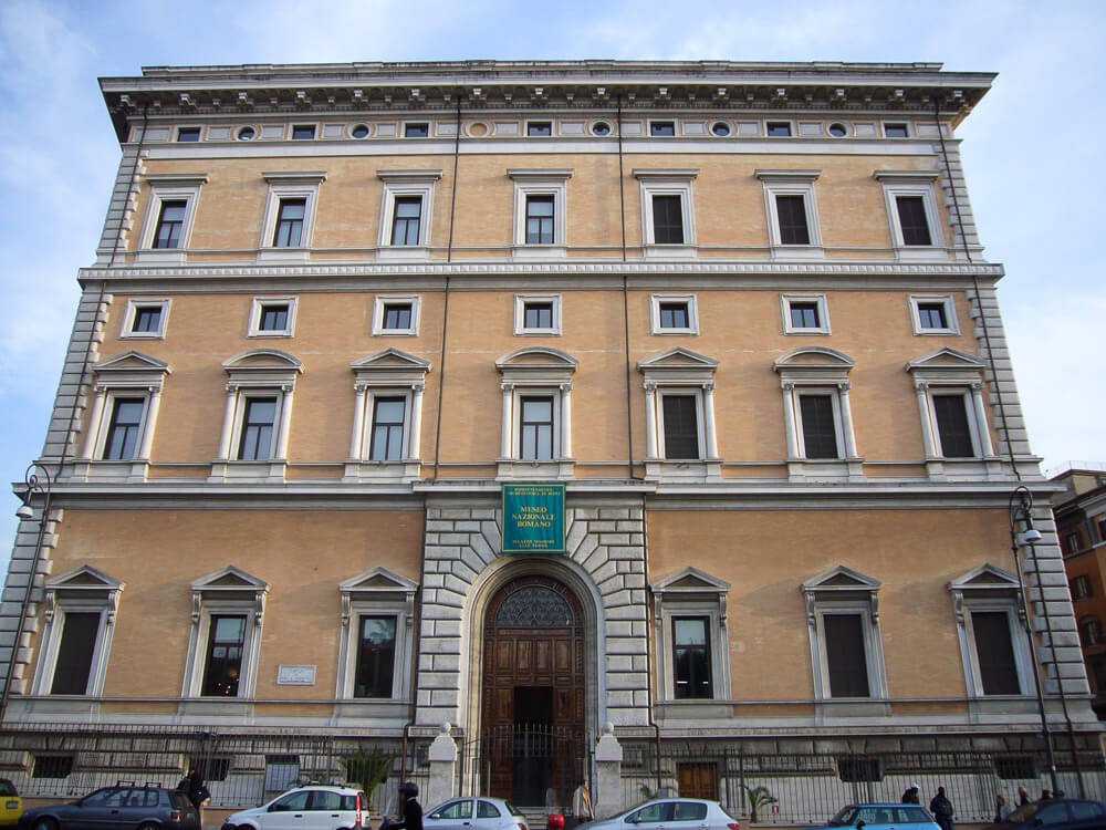 Fachada do Palazzo Massimo alle Terme, uma das sedes do Museu Nacional Romano, com paredes laranja e várias janelas.