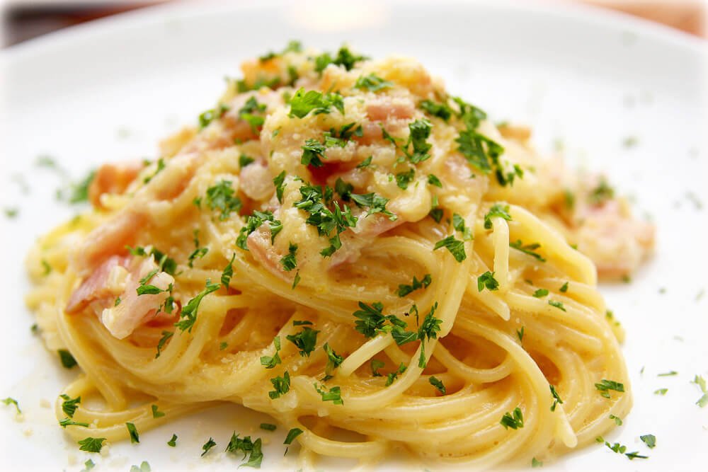 Prato branco com uma porção de pasta carbonara.