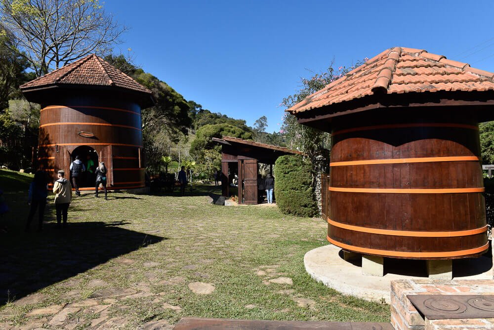 Gramado da cachaçaria A Bodega com casinhas cilíndricas feitas de madeira.