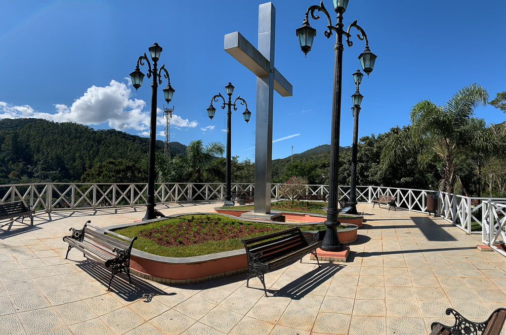 Mirante Cruzeiro com uma cruz no centro, postes com luminárias antigas e alguns bancos de madeira.