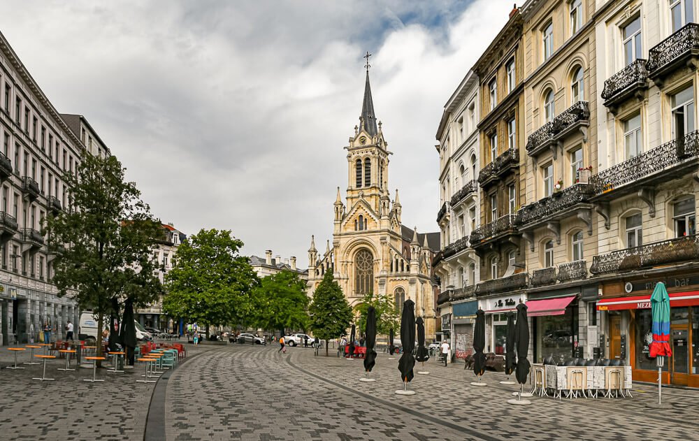 Praça Parvis de Saint-Gilles com restaurantes, árvores e uma igreja.