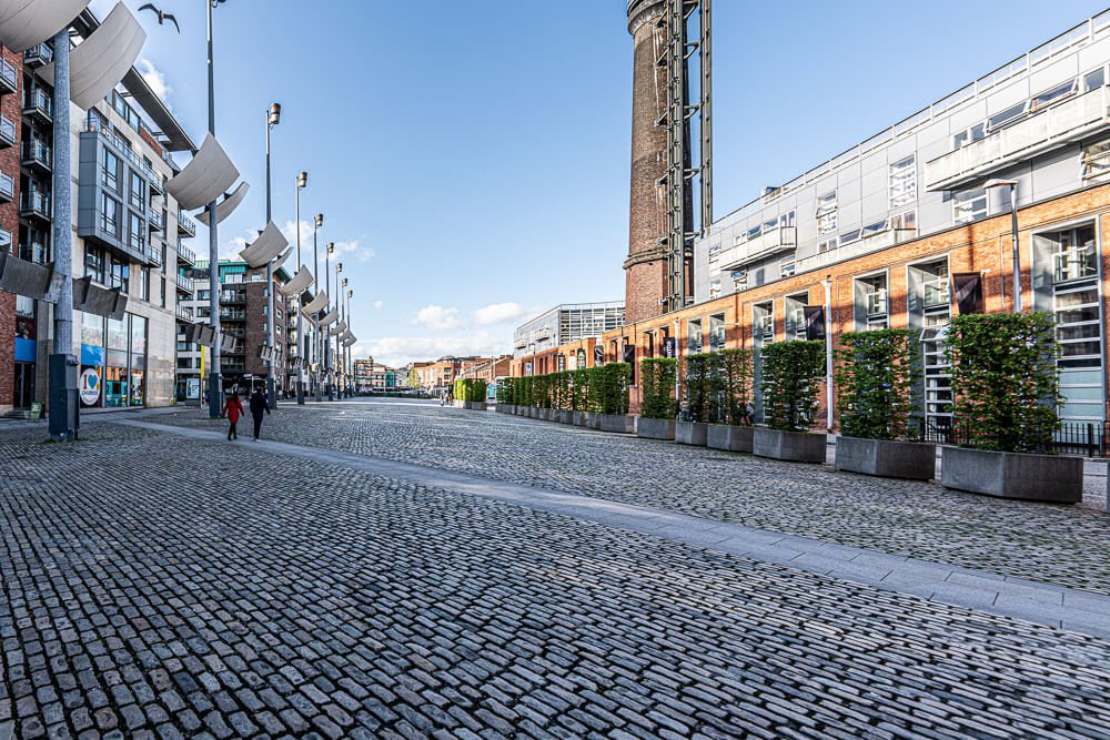 Smithfield Square com prédios, plantas decorativas e algumas pessoas caminhando pela praça.