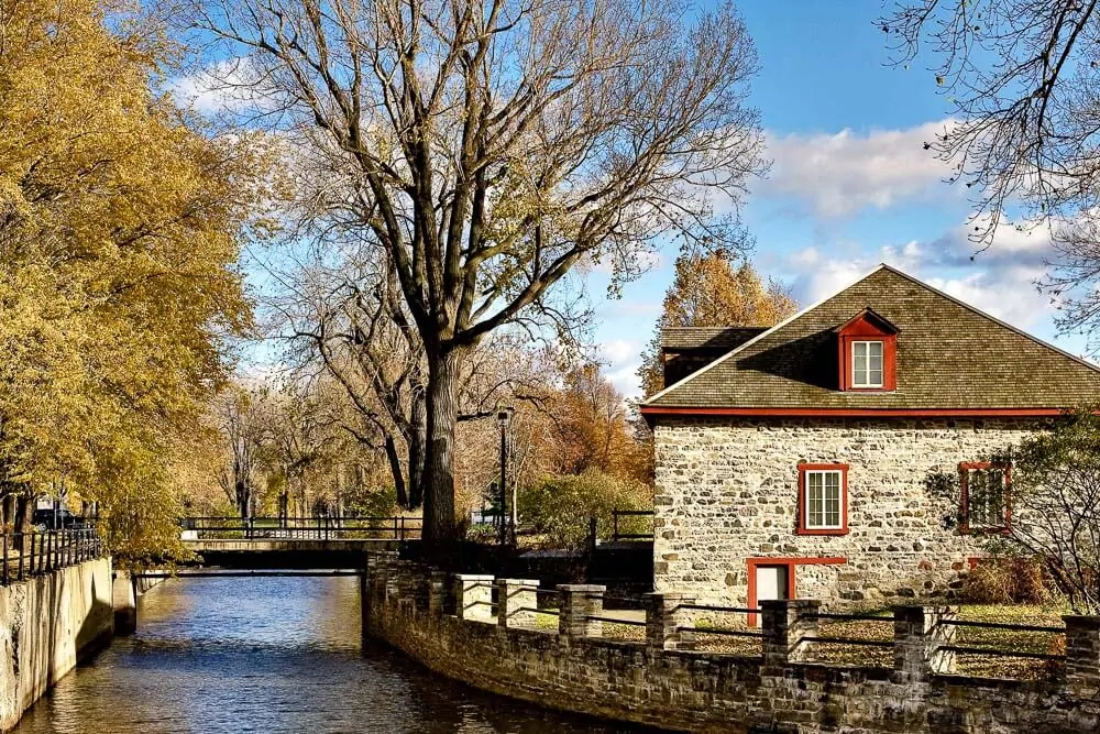 Casa com parede de pedras e muitas árvores, às margens do Canal de Lachine, em Montreal.