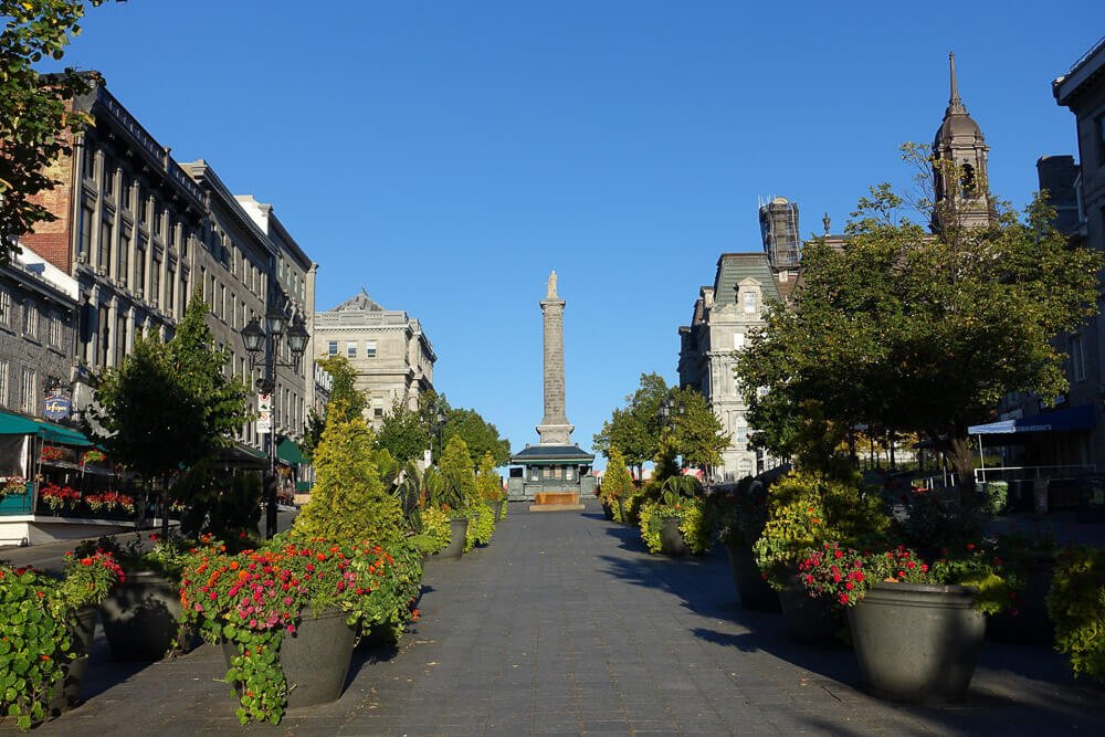 Praça Jacques-Cartier com vários vasos de plantas e um monumento ao centro.