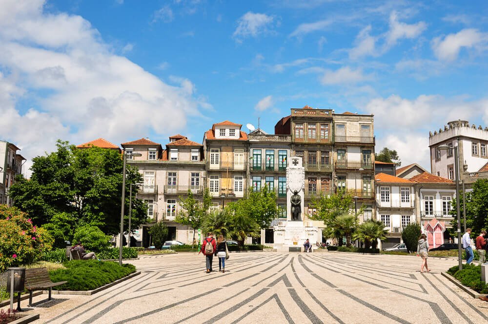 Praça de Carlos de Alberto com estátua, árvores e prédios ao fundo, na região de Cedofeita.