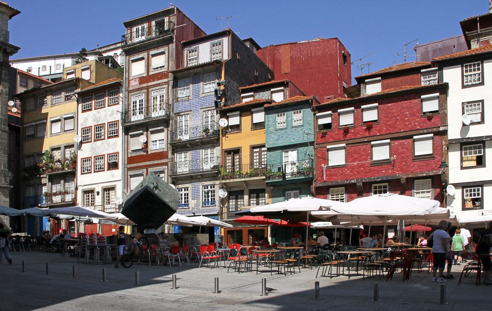 Praça da Ribeira com prédios coloridos, muitas cadeiras e guarda-sóis.
