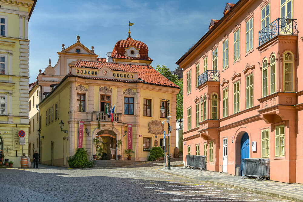 Rua Tržiště com chão de paralelepípedos e prédios com fachadas claras.