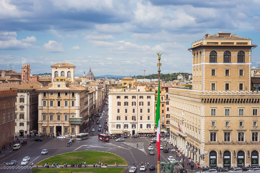 Vista superior para a Piazza Venezia e a Via del Corso, na região de Campo Marzio. Há muitos carros transitando pelo local.