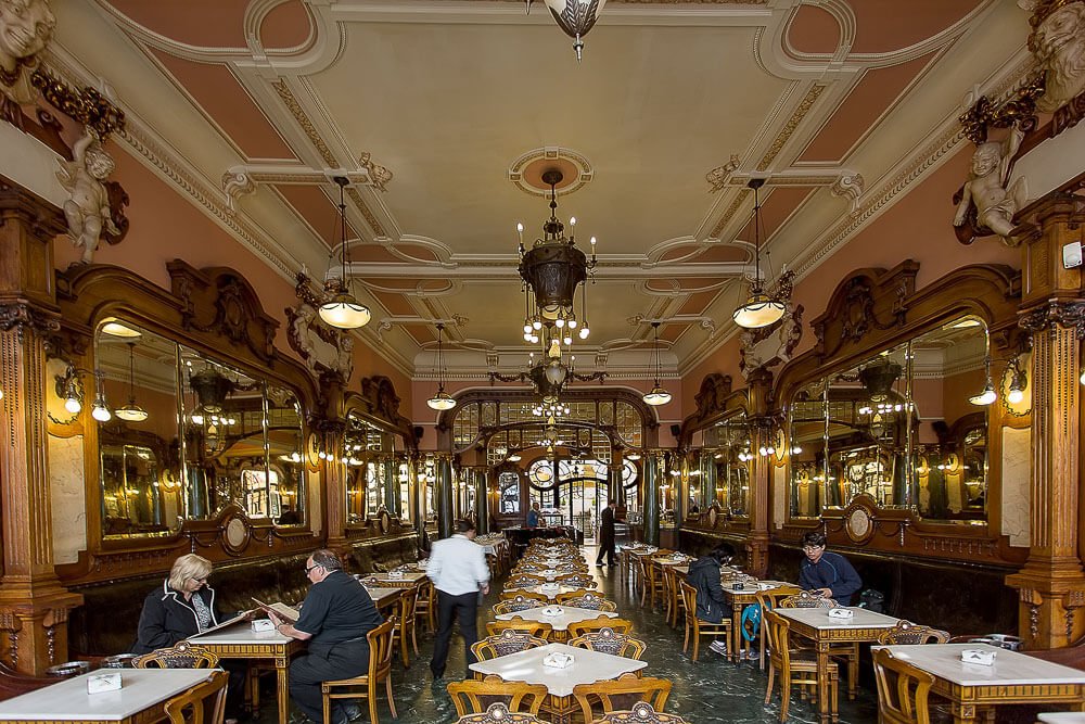 Salão interno do Café Majestic, com mesas, cadeiras, espelhos e lustres.