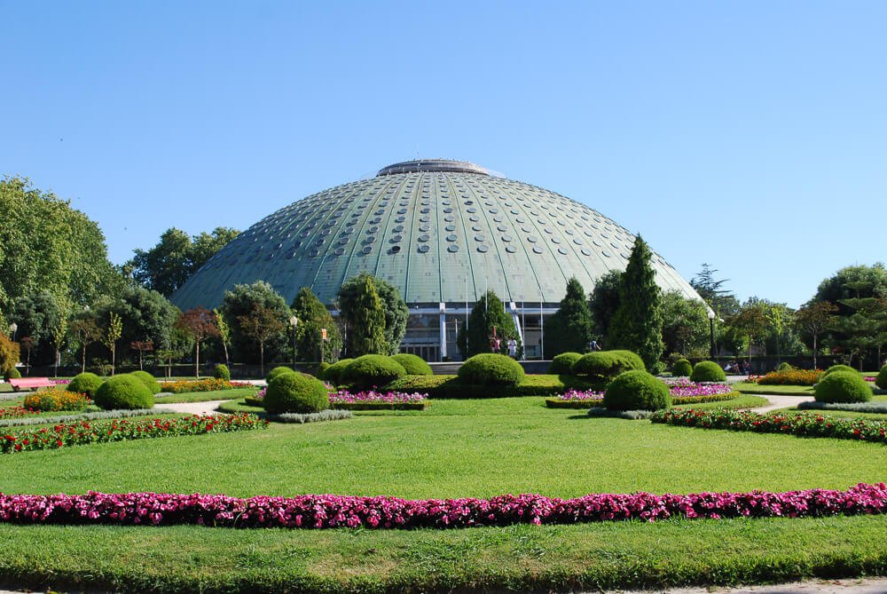 Jardim do Palácio de Cristal, com muitos arbustos, pequenas árvores e uma estufa no centro.