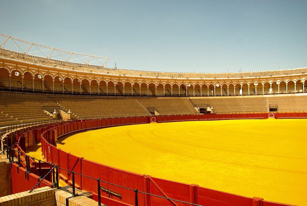 Arena de tourada da Real Maestranza, com chão amarelo e arquibancadas.