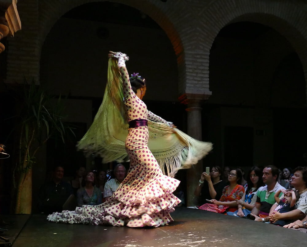 Dançarina de Flamenco se apresentando em um palco com uma pequena plateia à direita.