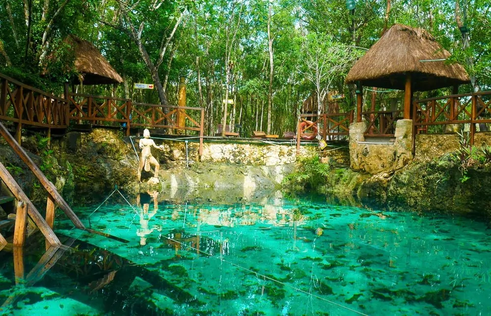 Cenote Zacil-Ha, com águas claras, esverdeadas e pequenas barracas de palha ao redor.