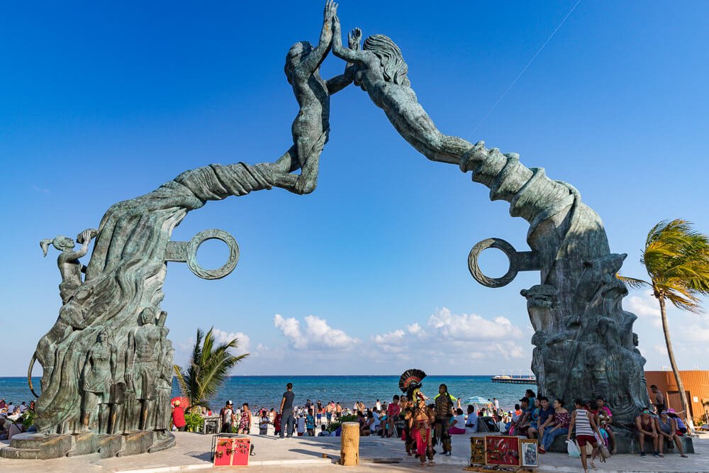 Escultura Portal Maya, com muitas pessoas abaixo do arco formado pelo monumento e o mar ao fundo.