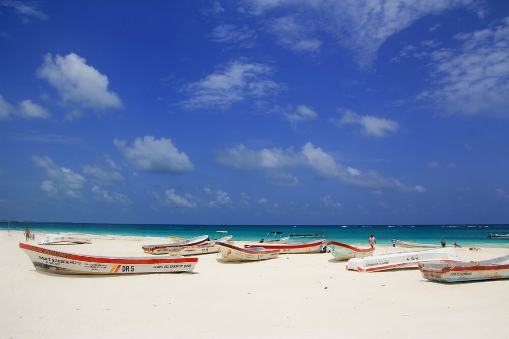 Playa Paraíso, com areia branca, vários barcos pequenos sobre a areia e mar ao fundo.