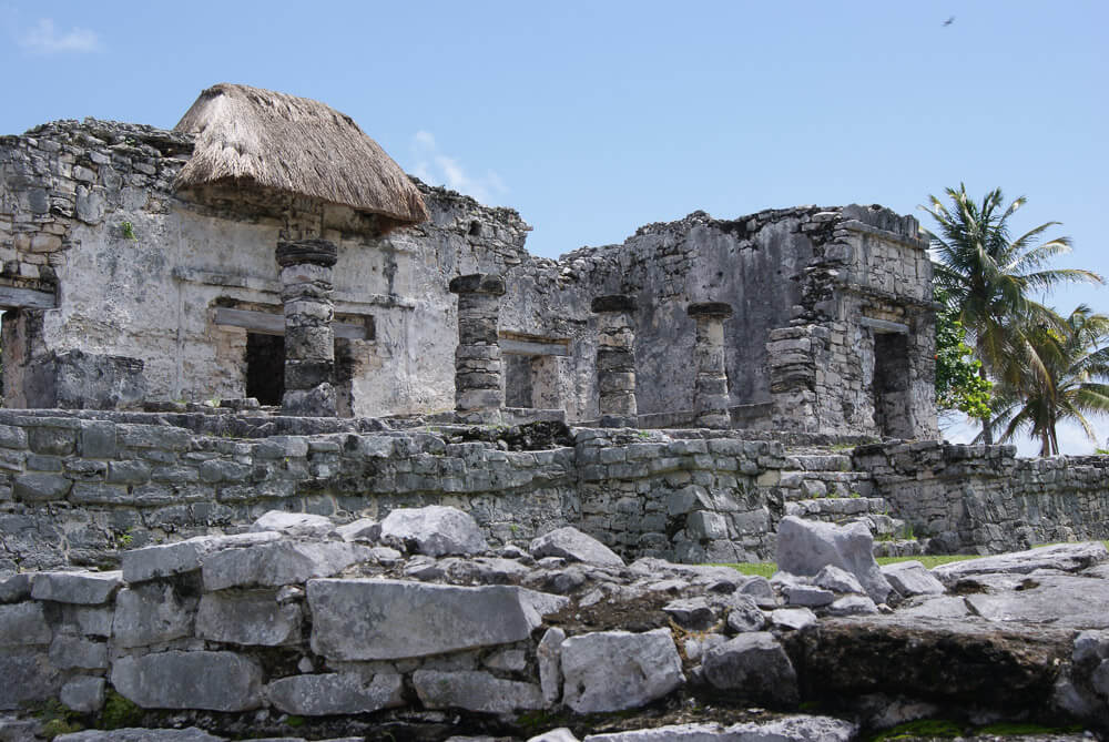 Templo del Dios Descendiente com estrutura de pedras cinzas e dois coqueiros à direita.