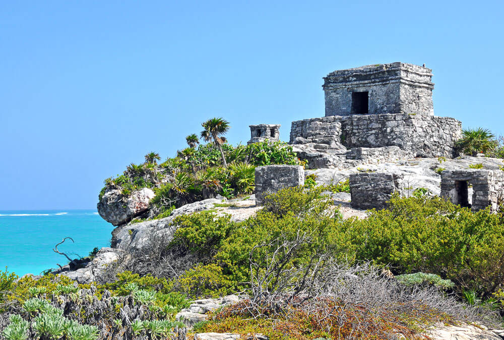 Templo del Dios Viento com estrutura de pedras, uma pequena vegetação e o mar à esquerda.