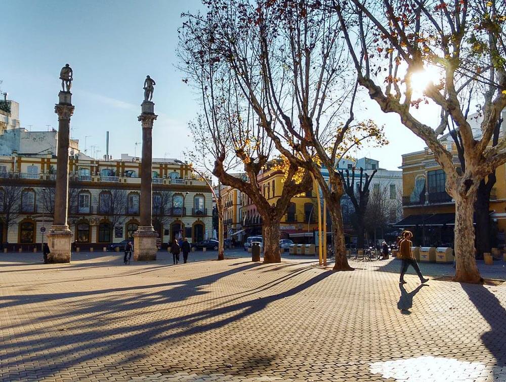 Alameda de Hércules com várias árvores, pessoas e prédios históricos nos arredores.