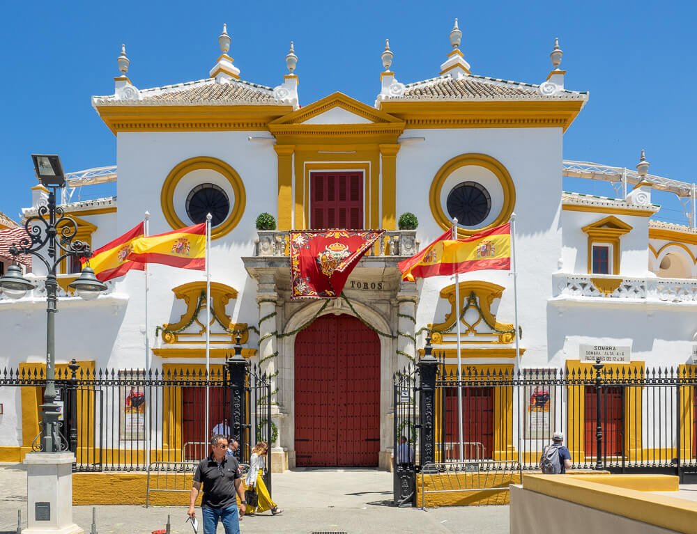 Fachada da Plaza de Toros de la Maestranza com prédio branco, amarelo e vermelho.