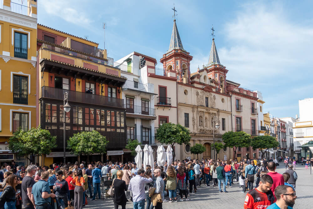 Plaza del Salvador com prédios pitorescos, árvores e muitas pessoas no local.