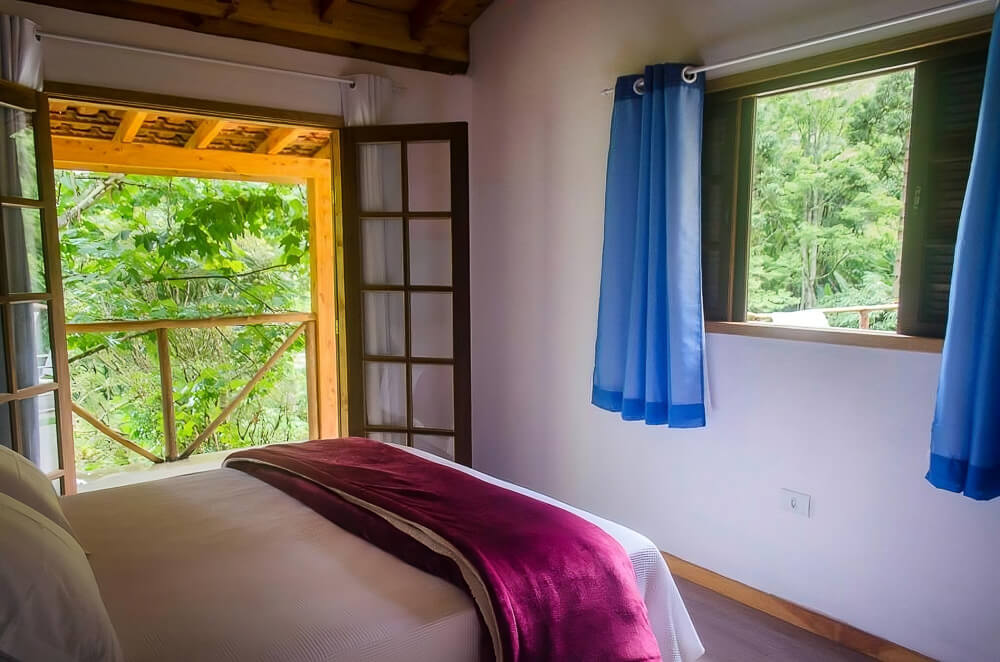 Quarta da pousada a Casa da Fazenda, com cama, varanda e janela com vista para a mata.