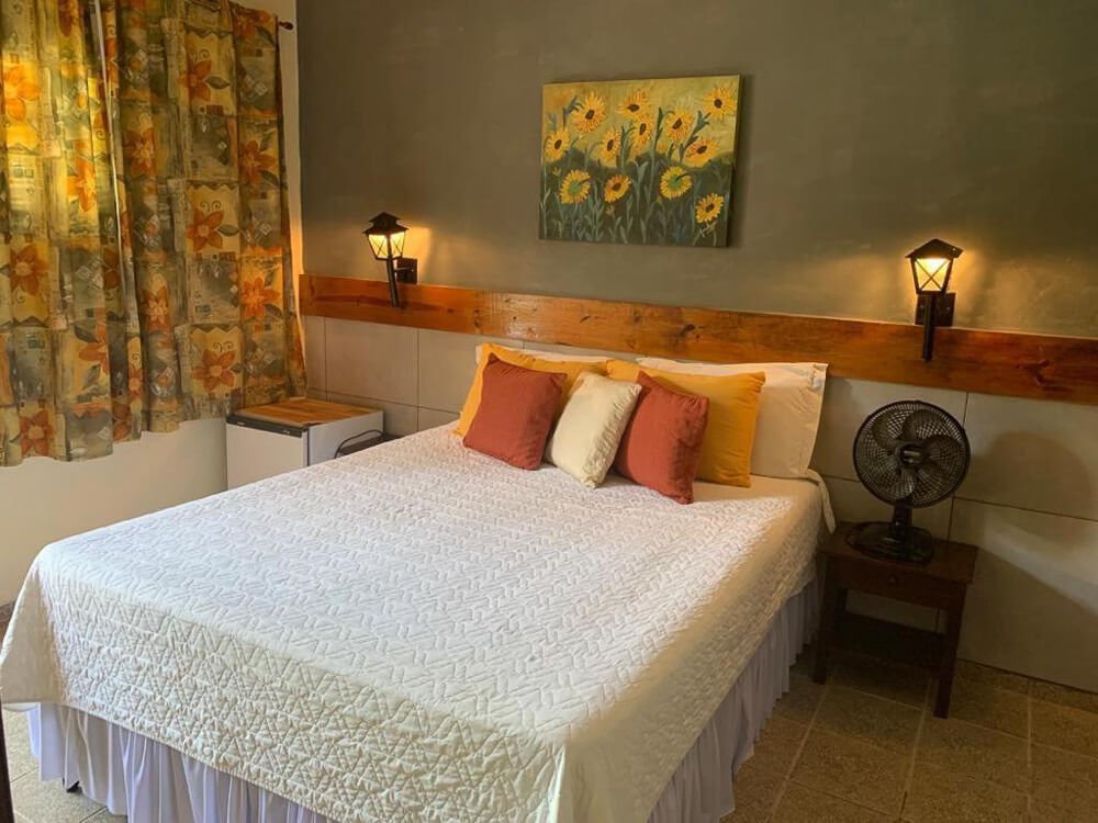 Quarto da Pousada do Grilo com cama, ventilador, luminárias e decoração charmosa.