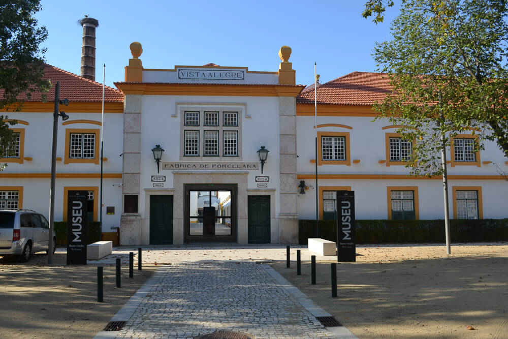 Entrada do Museu Histórico da Vista Alegre, com fachada branca e laranja, árvores e um caminho de pedras.