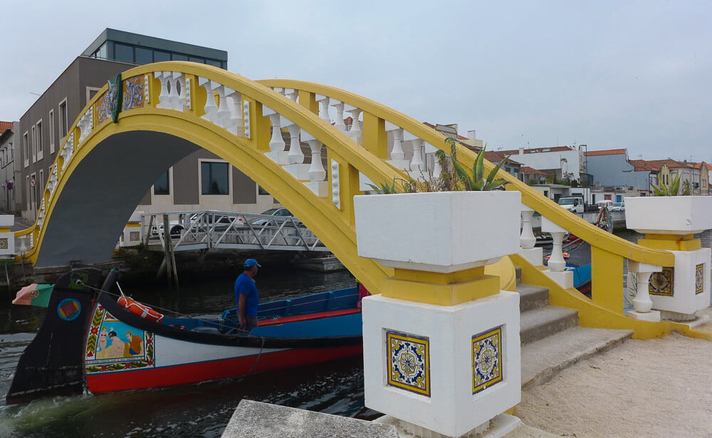 Ponte dos Carcavelos, com corrimão amarelo e barco moliceiro abaixo.