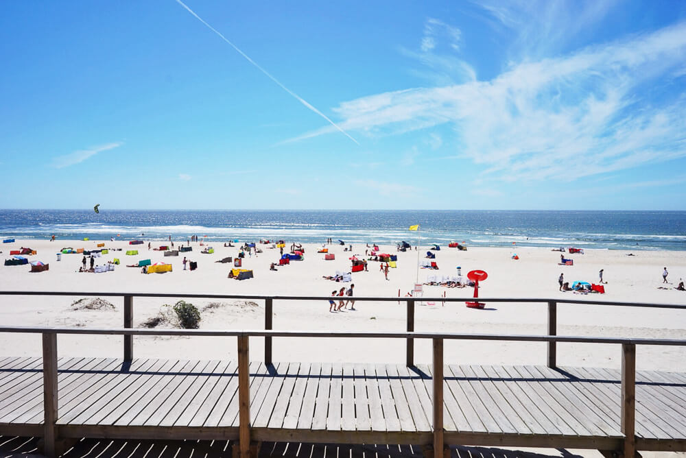 Praia da Barra com passarela de madeira e vários banhistas na areia clara.
