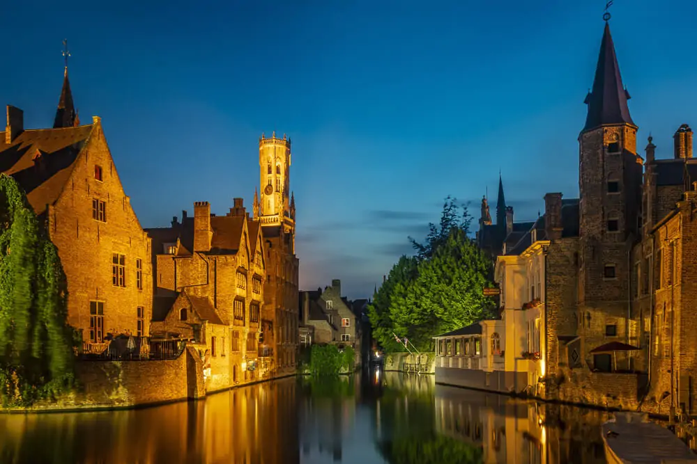 Canal em Bruges iluminado à noite e cercado por prédios históricos.