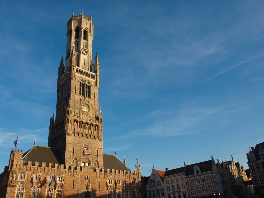 Campanário de Belford, em Bruges, com uma torre medieval e prédios nos arredores.