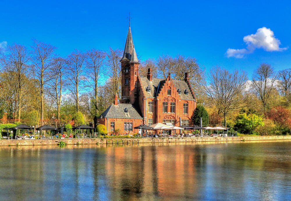 Castillo de La Faille, no Minnewater, com torre e várias árvores às margens do lago.