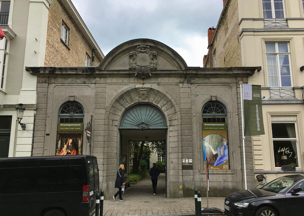 Fachada do Museu Groeninge, com porta em arco e carros estacionados em frente.