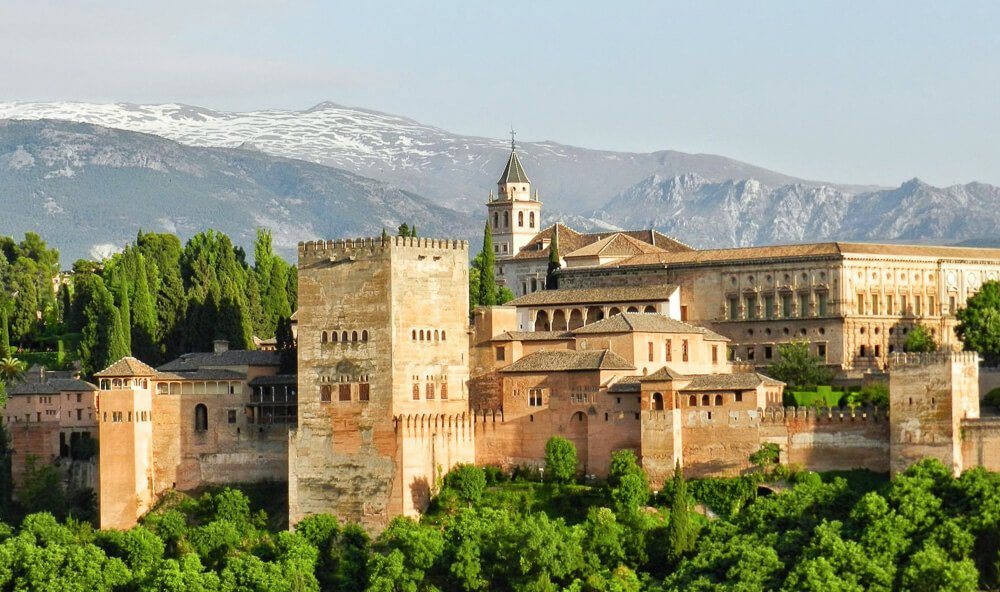 Alhambra cercada de árvores e montanhas ao fundo.