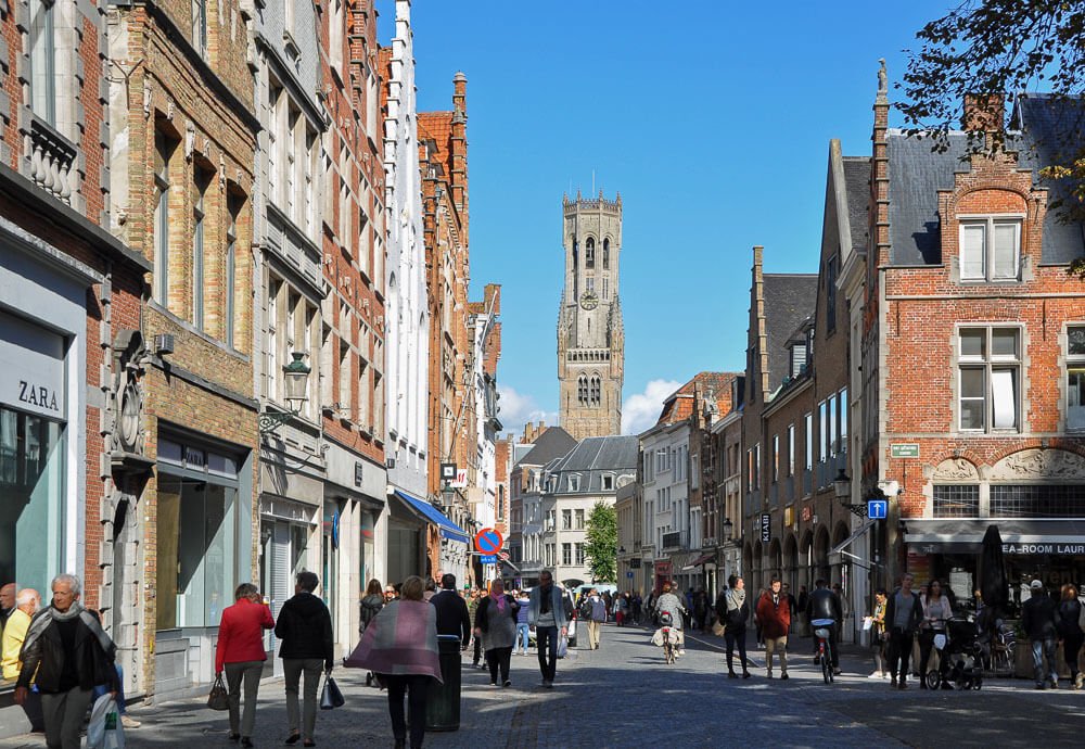 Rua Steenstraat, com várias lojas, prédios, pessoas e o Campanário de Belford no fundo.