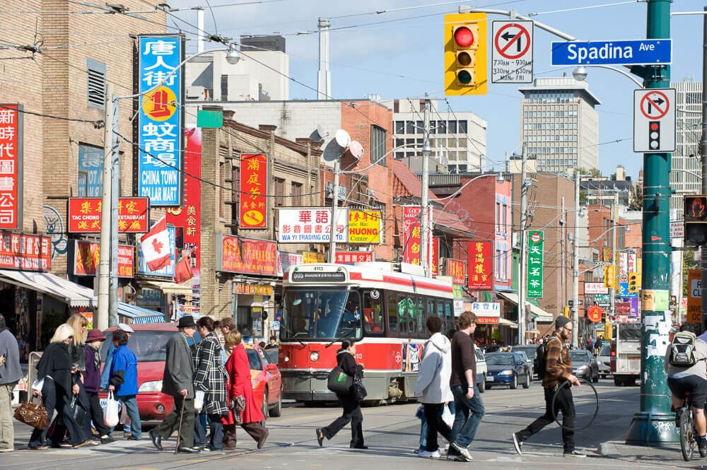 Avenida Spadina, com carros, trens, pedestres e estabelecimentos chineses, em Toronto.