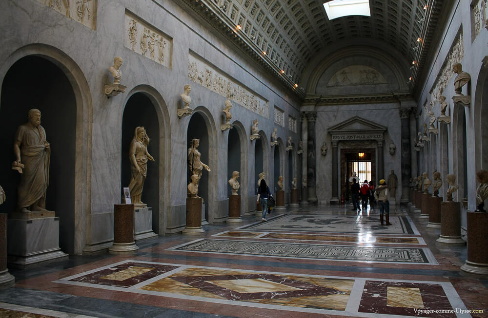 Salão interno da Galeria Braccio Nuovo com esculturas nas laterais e alguns visitantes no local.