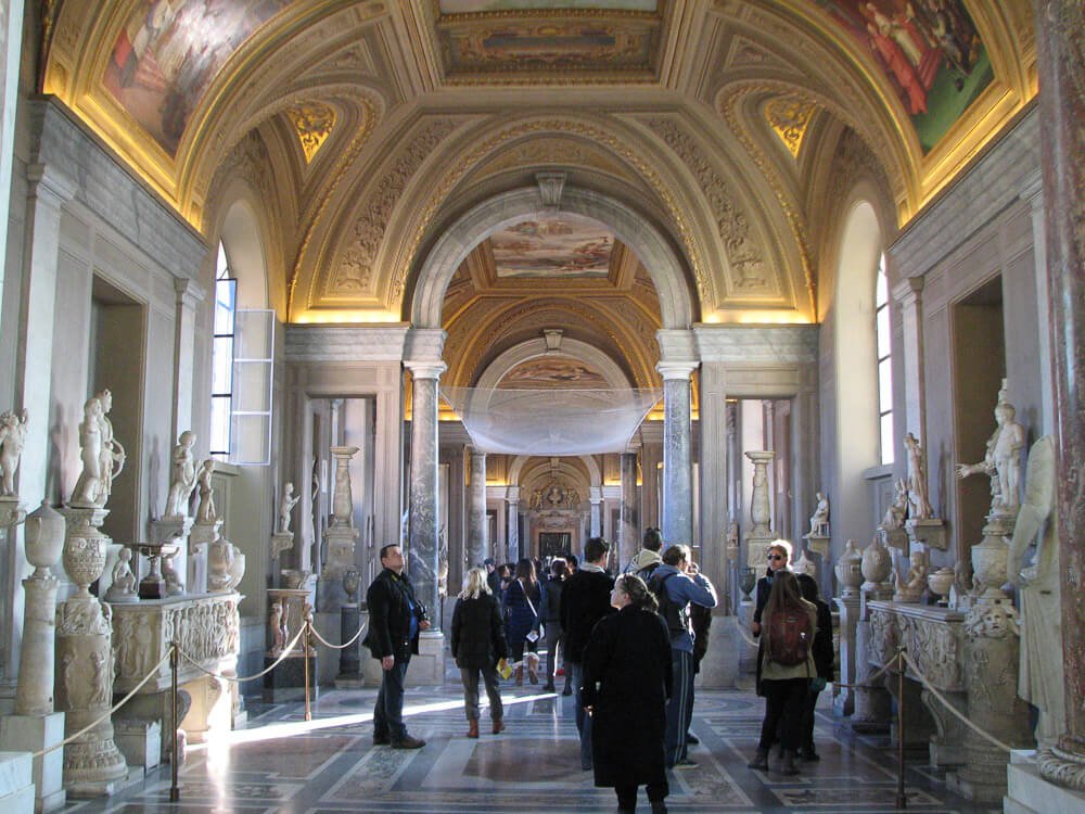 Interior da Galeria dos Candelabros, com várias esculturas, pinturas no teto e algumas pessoas.