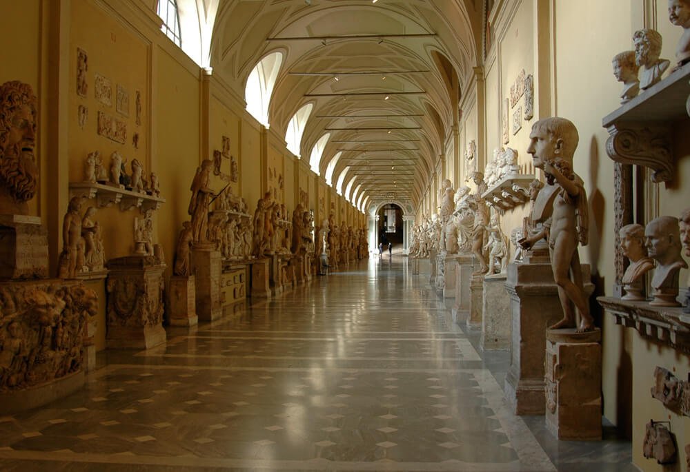 Corredor dentro do Museu Chiaramonti, com várias esculturas nas laterais e um teto curvado.