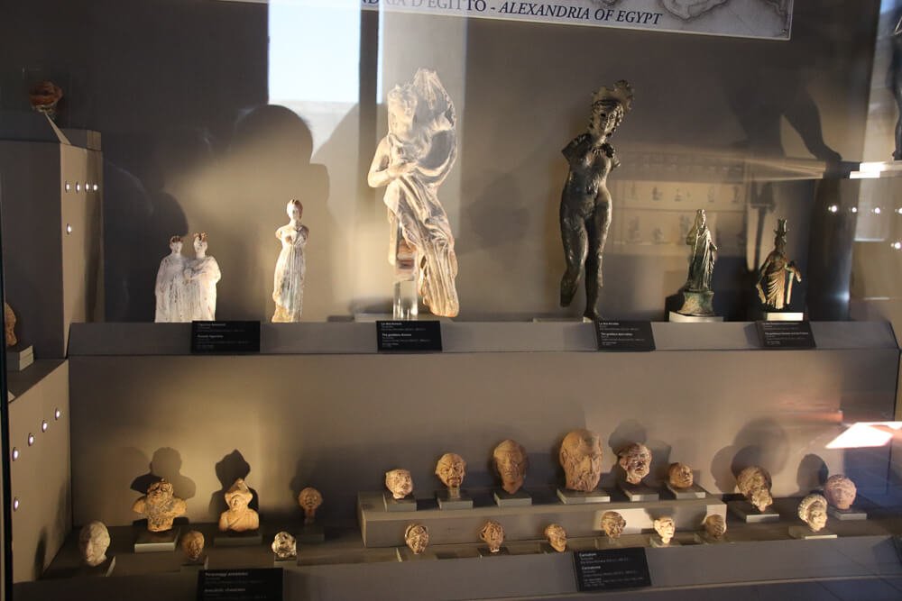 Vitrine com pequenas esculturas e fundo escuro, no Museu Gregoriano Egípcio.