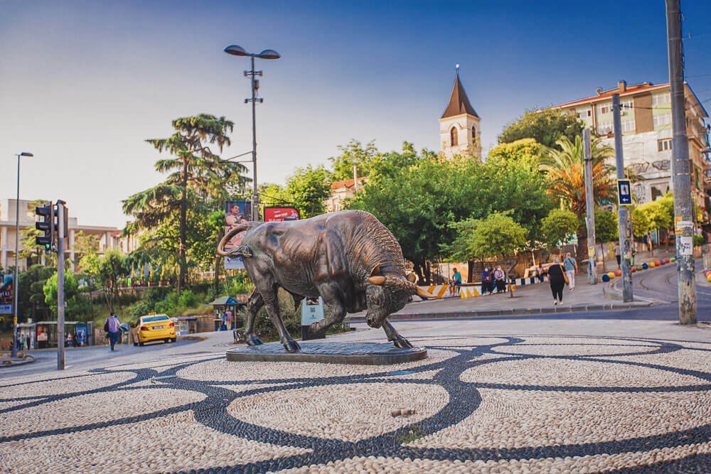 Estátua do Touro, em Kadıköy, com várias árvores e alguns edifícios históricos ao redor.
