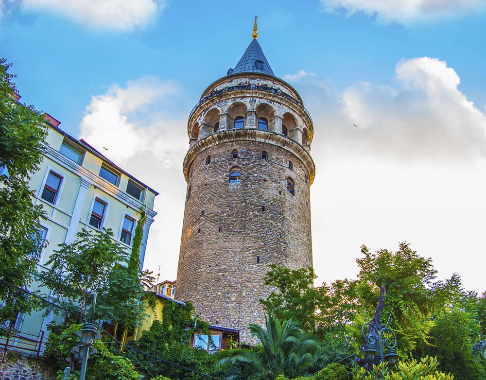 Torre Galatas, com paredes de pedras antigas, um prédio à esquerda e árvores nos arredores.