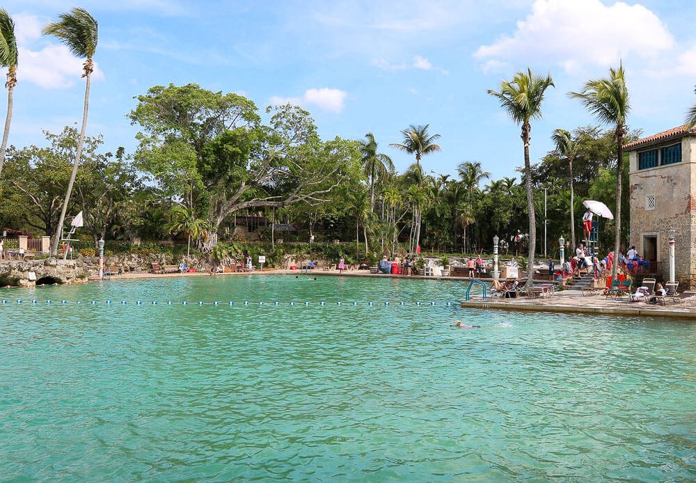 Venetian Pool, em Coral Gables, com piscina grande, vários coqueiros e banhistas à beira da piscina.
