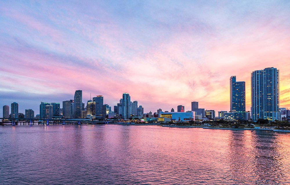 Litoral em Miami refletindo as cores do pôr do sol, com vários prédios à beira-mar.