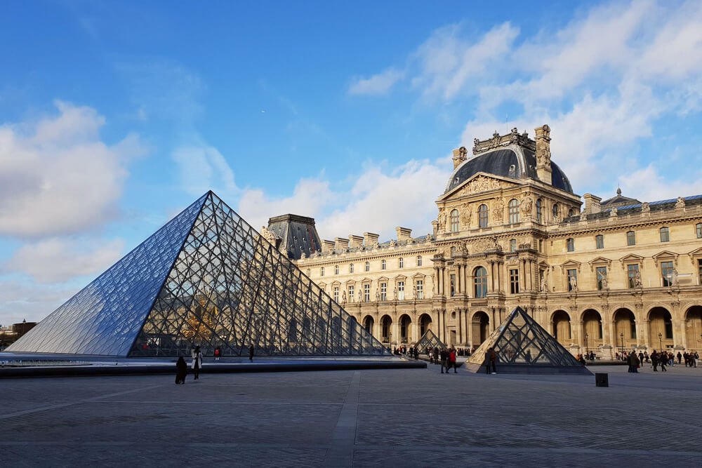Pátio do Museu do Louvre, com algumas pessoas caminhando pelo local.