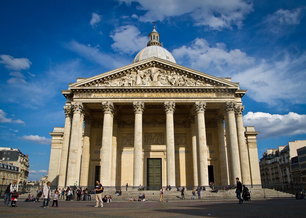 Fachada do Panthéon, com várias colunas e pessoas caminhando em frente.