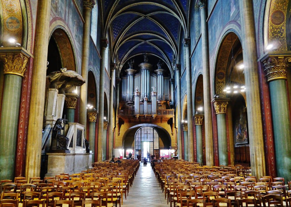 Interior da Catedral Saint-Germain-des-Prés, com muitas cadeiras, teto curvado e decoração em tons de verde e azul.