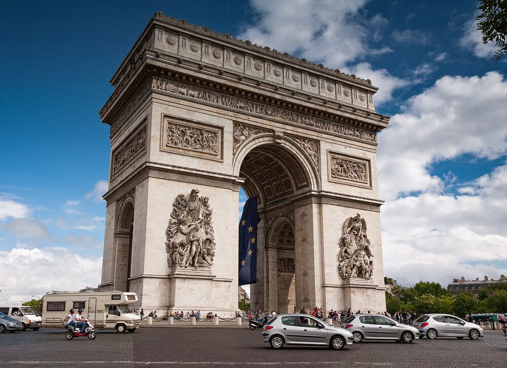 Arco do Triunfo, com várias motos e automóveis circulando pela rua em frente.